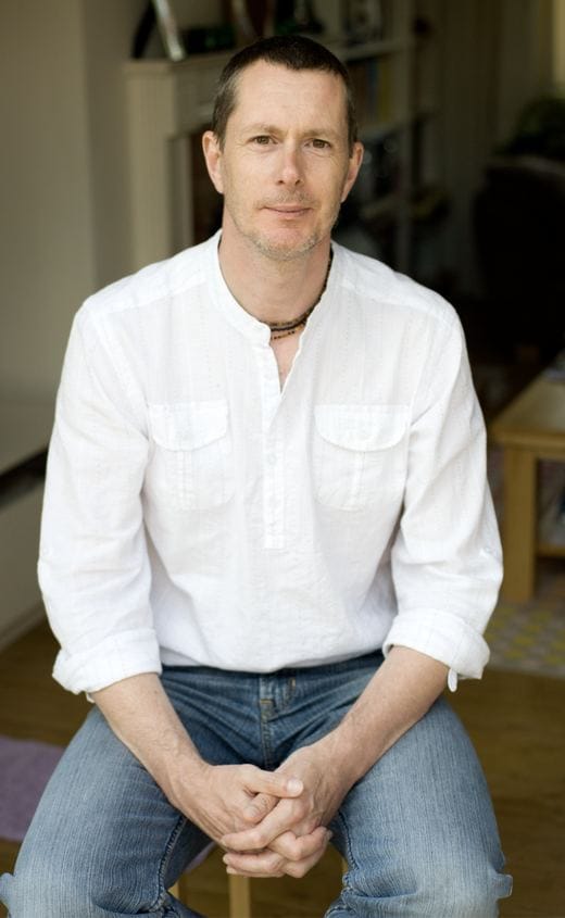 Portrait of Ken Banks seated, wearing a white shirt and jeans